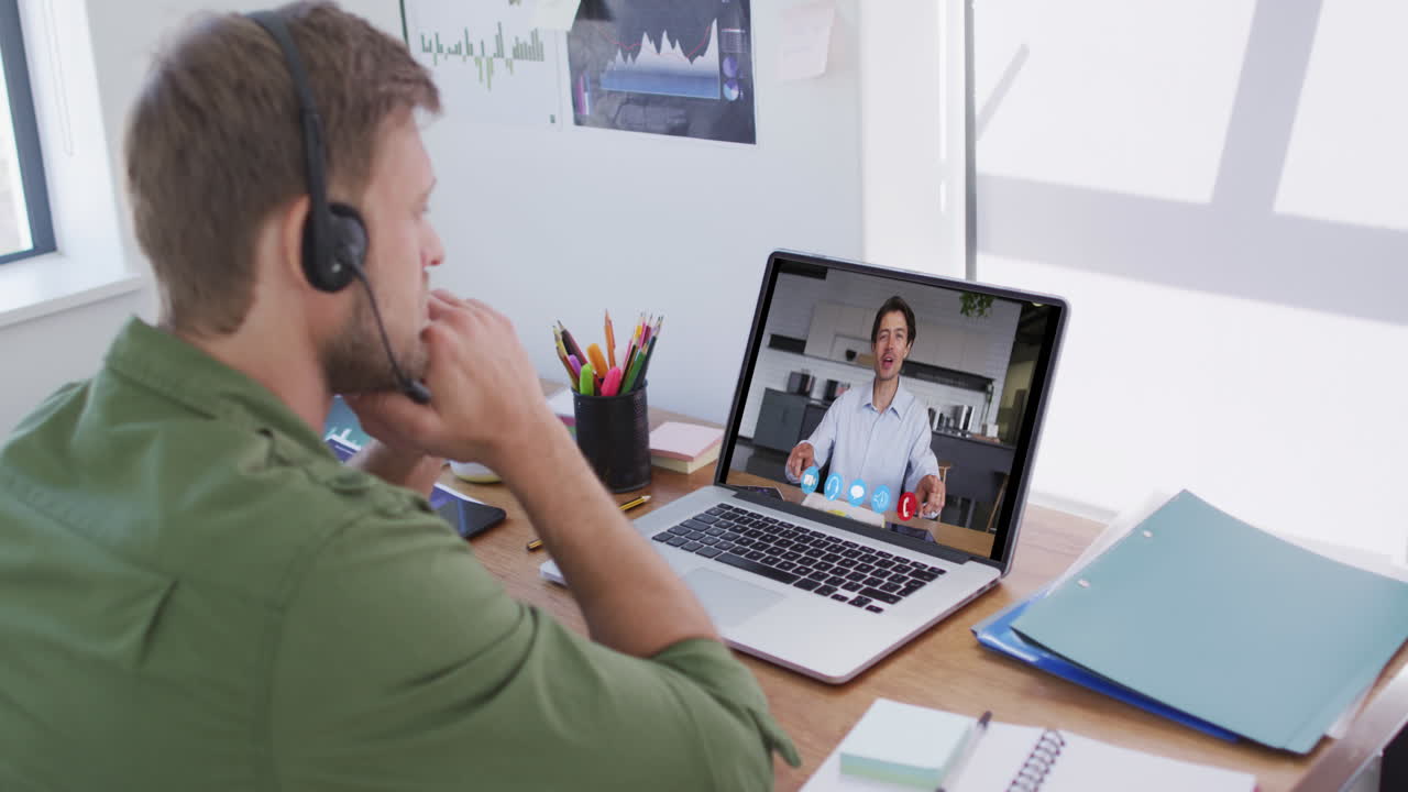 Kaukasisk mand bruger bærbar computer og telefonheadset på videoopkald med en mandlig kollega.