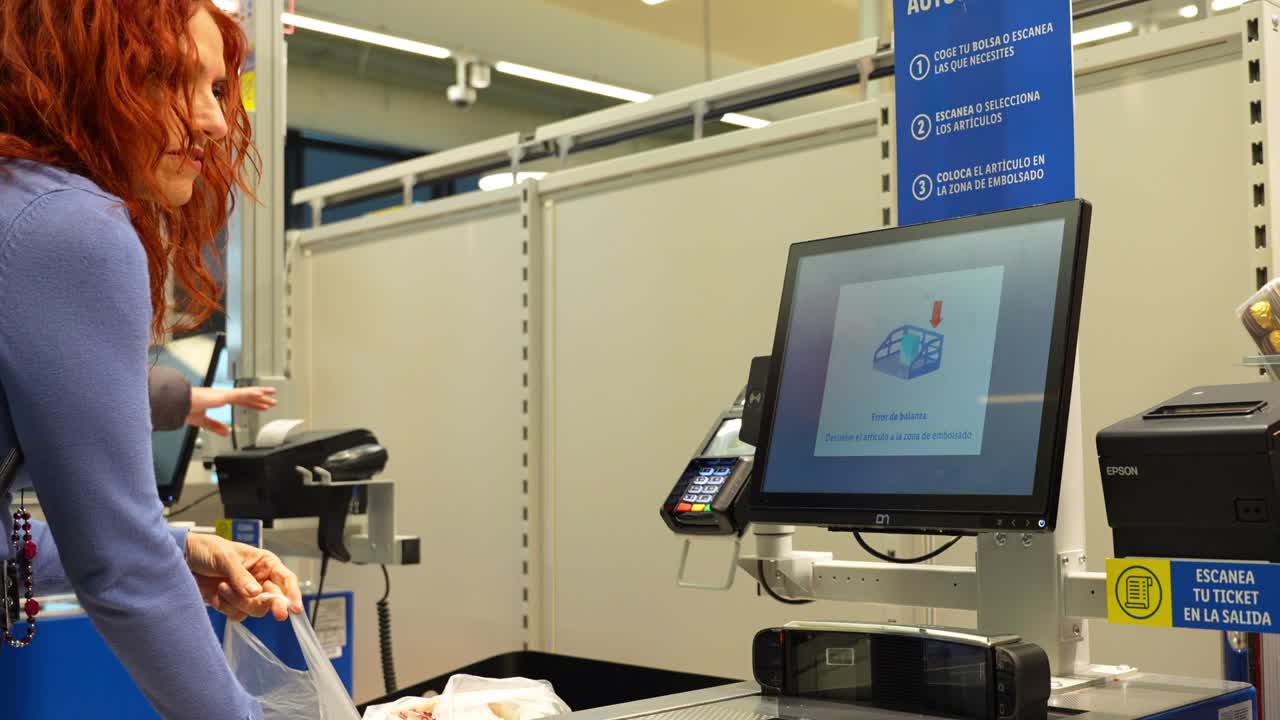 Woman scans final product at a supermarket self-checkout machine and bags her groceries