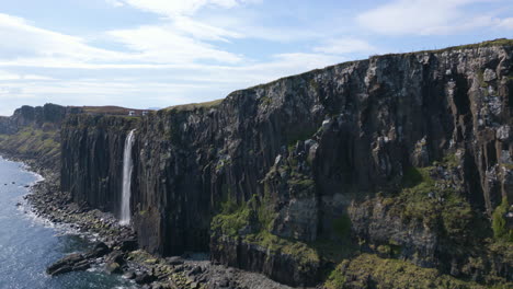 Cascada-De-Roca-Escocesa-Que-Cae-Desde-Acantilados-Hacia-El-Mar-Bajo-Un-Cielo-Azul-Brillante-En-La-Isla-De-Skye,-Escocia