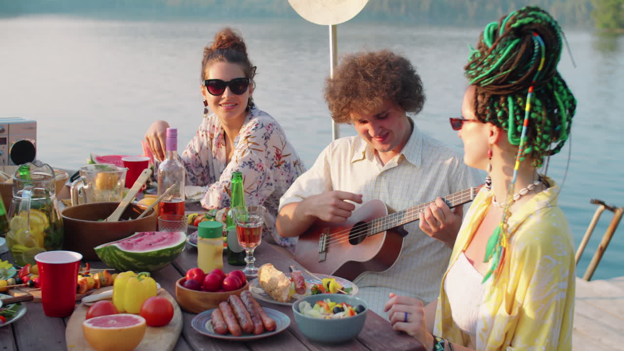 hombre feliz tocando el ukulele en una fiesta en el lago con amigos