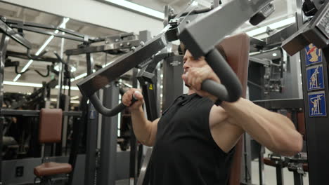 mascular man in 40th doing machine chest press exercise in modern gym