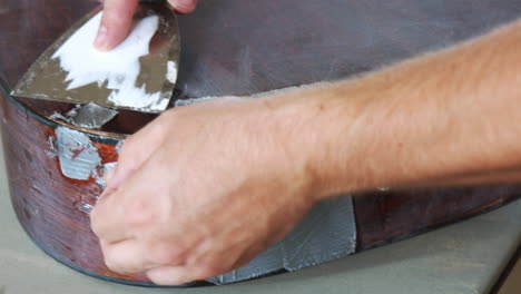 two hands scrape off duct tape off the bottom of an old guitar or broken or in disrepair