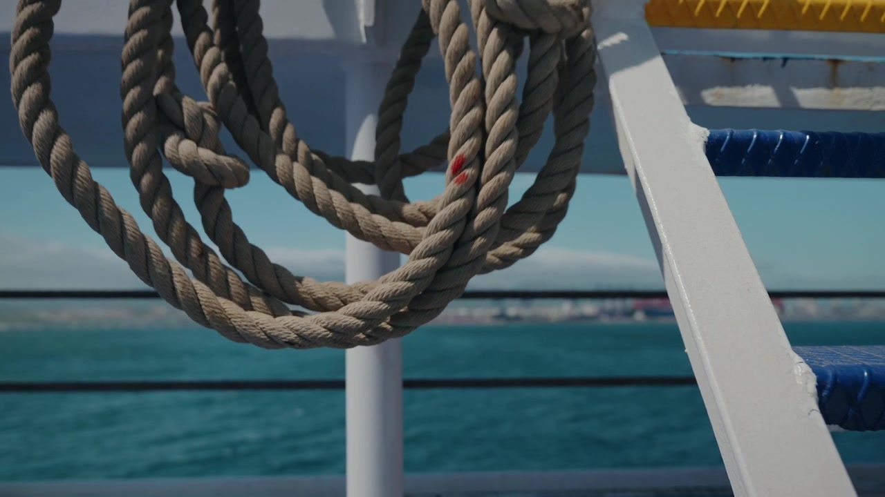 Corda nautica spessa e attorcigliata avvolta sulla ringhiera bianca di un traghetto sopra il mare blu.