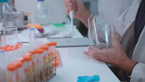 researcher filling sample tray with fluid substance from beaker using pipette at chemical laboratory