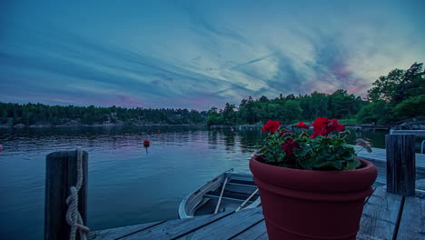 overview shot of a red potted flower on wooden pier along rocky slope beside a calm lake on in timelapse