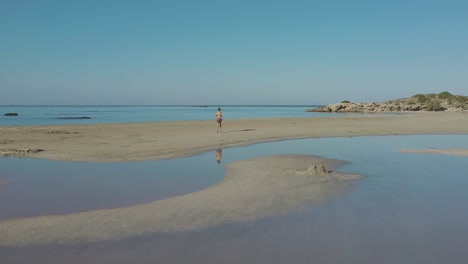 drone aerial view of woman running in elafonissi beach lagoon reflection