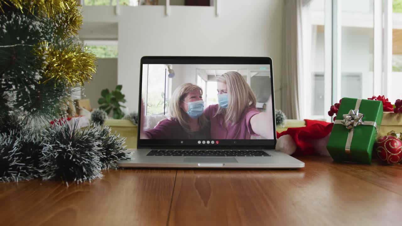 madre e hija usando máscaras faciales en una videollamada de navidad en una computadora portátil