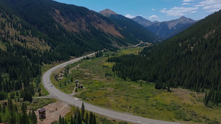 Strada di montagna che si snoda in un'ampia valle del Colorado con vegetazione lussureggiante, Million Dollar Highway Colorado USA