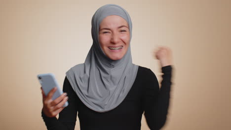 Happy-muslim-woman-use-mobile-phone-say-wow-yes-found-out-great-big-win-news-doing-winner-gesture