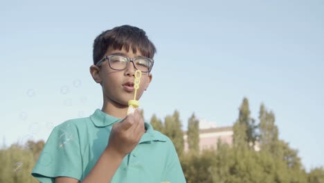 happy boy in eyeglasses blowing bubbles and laughing at the park