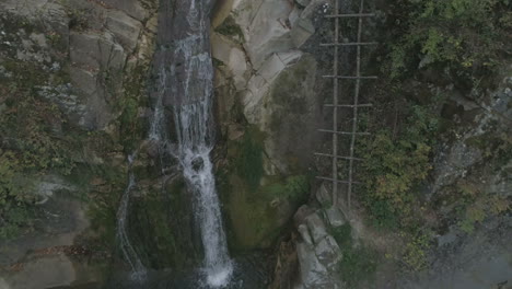 Aerial-footage:-a-small-stream-flows-into-a-high-waterfall-in-the-middle-of-the-woods