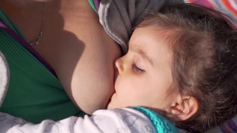 mother breastfeeding her baby girl on a sunny summer day