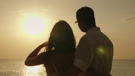 una pareja joven está admirando la puesta de sol sobre el mar vista trasera video 4k