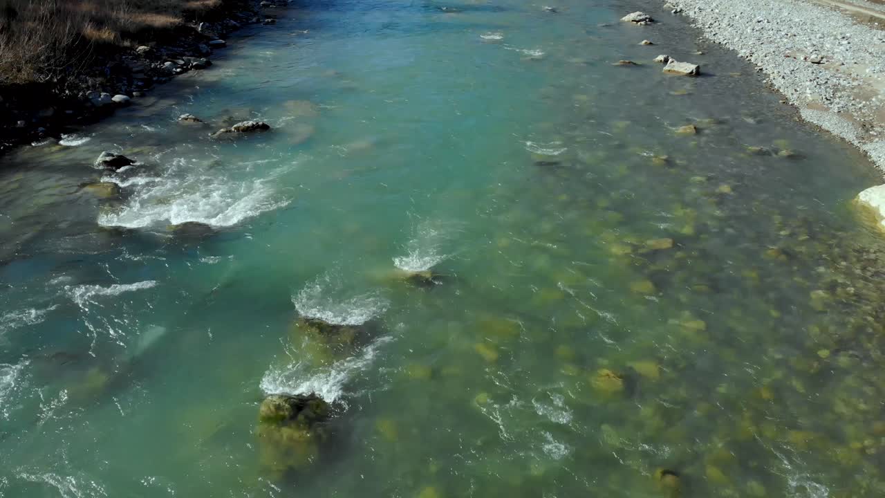River stream flowing water splashes with rocks and cliffs falling down through pebbles, aerial descending view, water texture