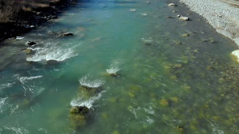 river stream flowing water splashes with rocks and cliffs falling down through pebbles, aerial descending view, water texture