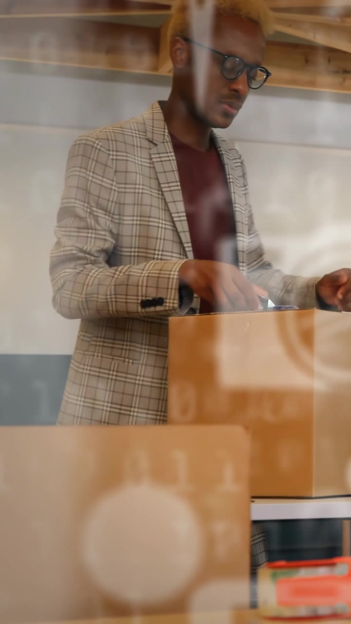 Vertical video: Man entering with box, sorting office boxes and holding clipboard, bokeh overlaying