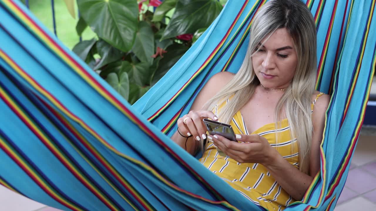mujer navegando por el teléfono inteligente y descansando en la hamaca