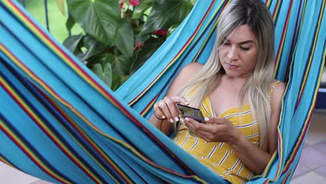 Mujer-Navegando-Por-Teléfono-Inteligente-Y-Descansando-En-Una-Hamaca