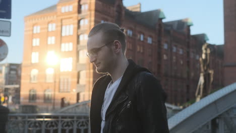 young european man with glasses and beard walking through city at golden hour