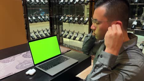 hombre millennial asiático que usa auriculares y disfruta de la música frente a una computadora portátil con pantalla verde