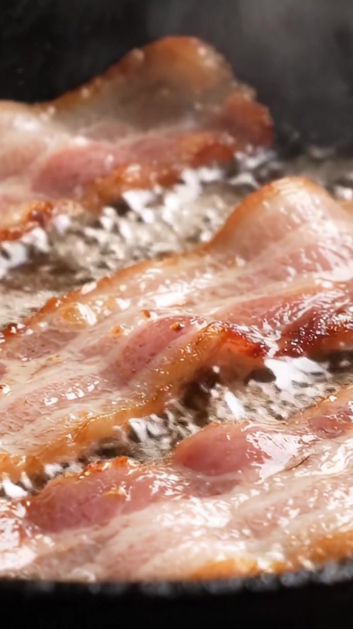 Spruttende bacon steger på en varm pande: Et nærbillede af perfekt sprøde strimler, der steger i herligt varmt fedt