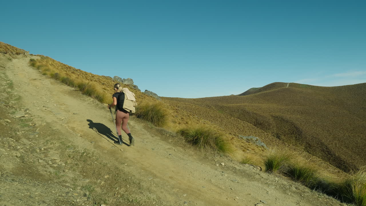 Woman hiking up steep slope of mountain trail in good condition with backpack