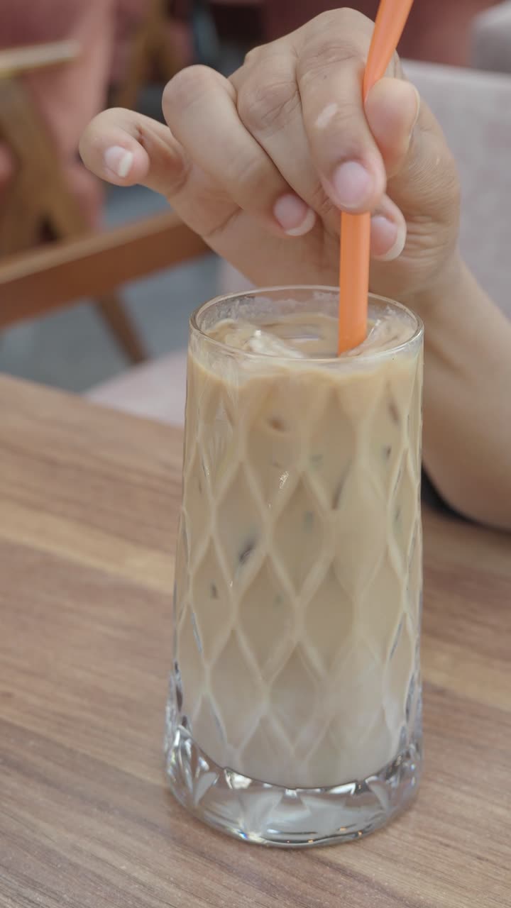 Primo piano di una mano che mescola un caffè freddo con una cannuccia