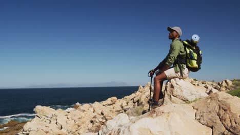 african american man hiking resting on a rock in countryside by the coast