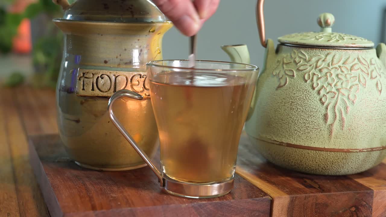 배경에 녹색 식물이 있고 유리 찻잔이 있는 밝고 바람이 잘 통하는 방에 있는 나무 테이블에 있는 녹색 찻주전자에 허브차 만들기