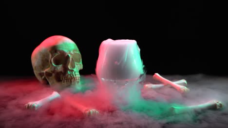cognac glassful with smoke near the skull and bones on a black background - cognac glassful with smoke near the skull and bones on a black background with red and green light at dark studio