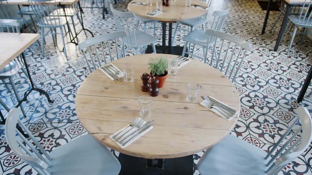 Elevated view of empty tables and chairs in a restaurant with tiled floor and feature window and stone wall, handheld