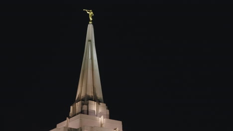 golden statue on spire of lds mormon temple church building at night illuminated by warm light in gilbert, arizona