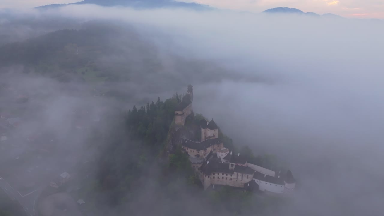 Drone shot of Orava Castle shrouded in dreamy fog at sunrise