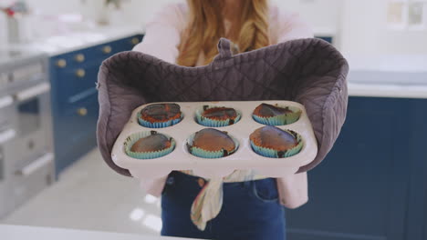 portrait of teenage girl taking out tray of burnt homemade cupcakes from the oven at home