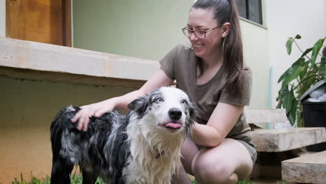 Mujer-Con-Gafas-Y-Su-Perro-Pastor-Australiano-Disfrutando-De-Un-Momento-Juntos-En-Su-Jardín,-Ella-Felizmente-Le-Da-Un-Baño