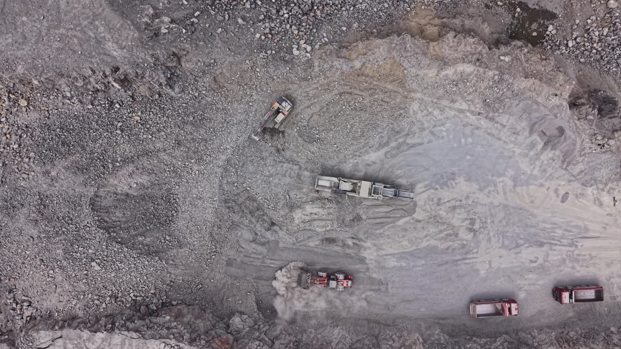 Construction vehicles operate in a gravel pit during daytime work hours
