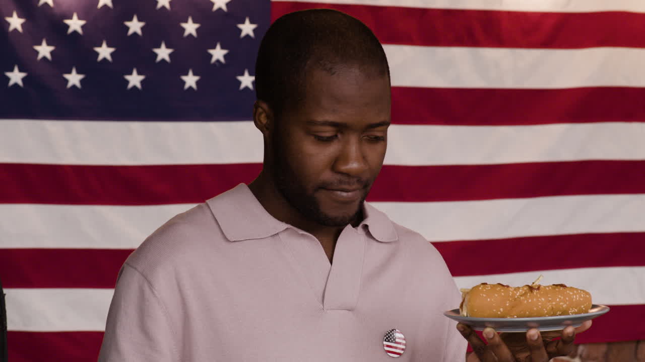 Man eating a hot dog in front of the American flag