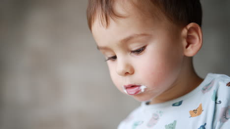 lovely caucasian baby boy's face with dairy around his mouth. close up. kid eating yogurt at home. blurred backdrop.