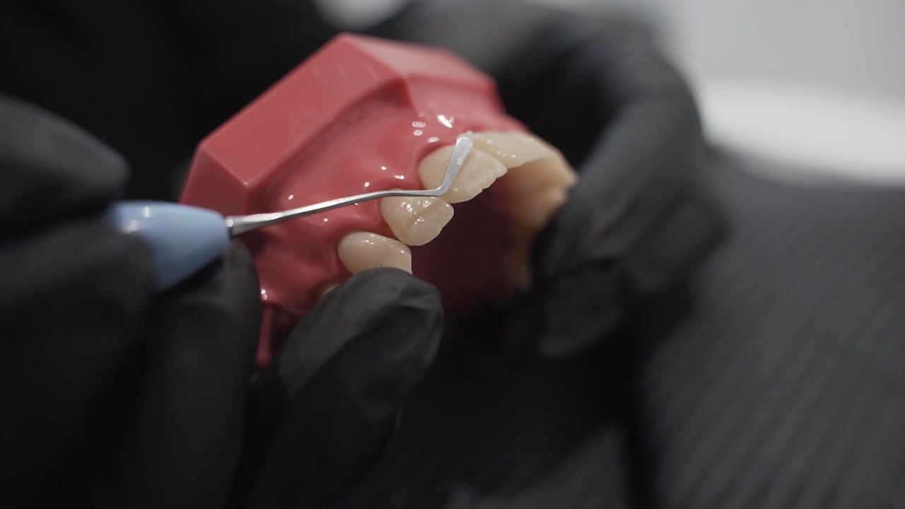 dental technician adjusts a veneer on a tooth model with precision instruments