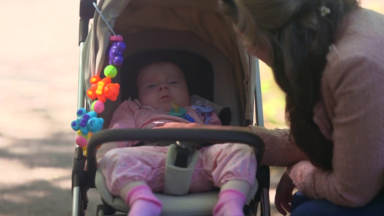 Young mother gently interacting with her infant seated in a stroller during an outdoor walk