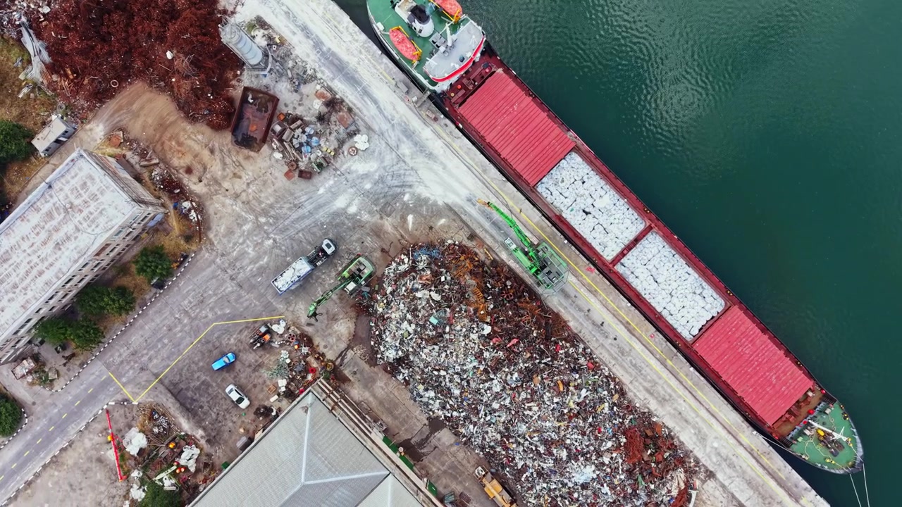 Vista di un porto con una nave da carico e cumuli di rottami metallici di giorno, con operai e attrezzature nelle vicinanze