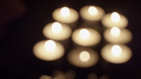 Group-of-defocused-tea-candles-burn-in-dark-background,-copy-space