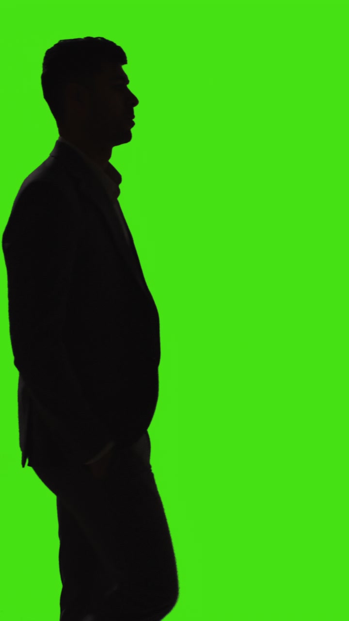Vertical Video Silhouette Of Businessman Wearing Suit Walking Across Frame Against Green Screen Background 1