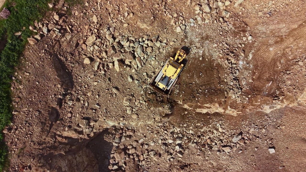 Luftfoto ovenfra af en stationær gul bulldozer i et stenet stenbrud.