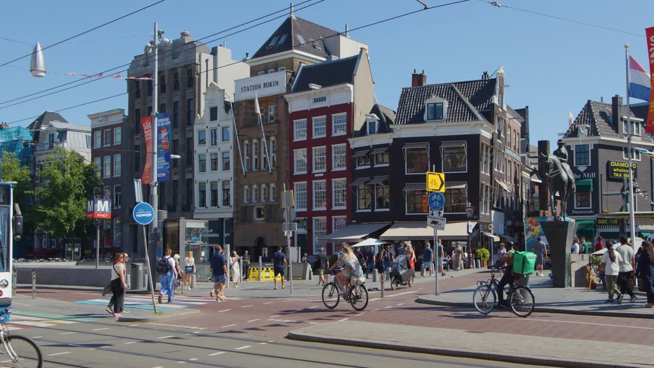 Daytime tram passes cyclists and pedestrians at urban Amsterdam intersection, historic buildings, clear weather