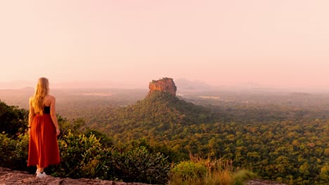 a serene and cinematic aerial clip of a woman standing on pidurangala rock, gazing at the sunrise over the majestic sigiriya rock.