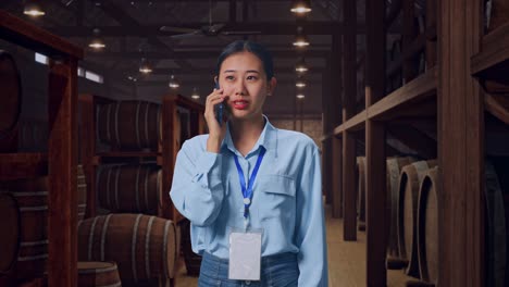 asian female professional worker standing in cellar of winery, she pick the phone up and started to speaking with it
