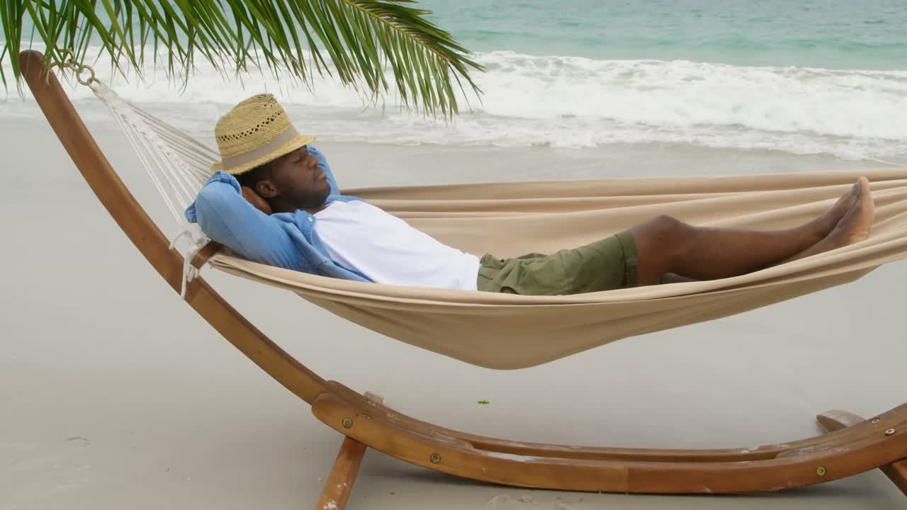 Side view of African american man sleeping in a hammock on the beach 4k
