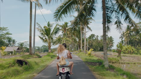 travel couple riding scooter on tropical island happy woman celebrating with arms raised enjoying fun vacation road trip with boyfriend on motorbike rear view