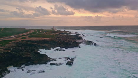 surf breaking rocky beach under sunset cloudy sky aerial shot. turbulent sea